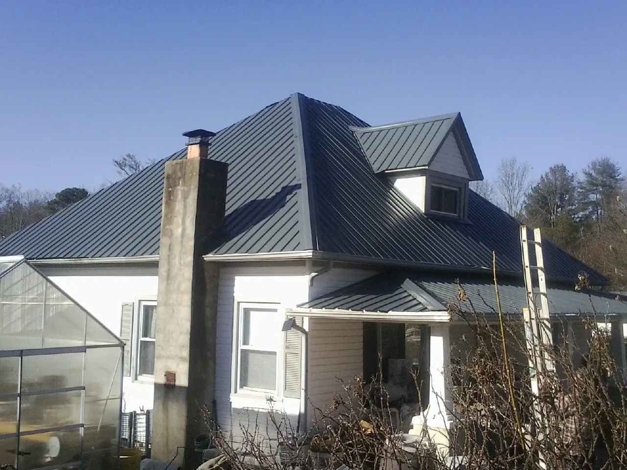 Dark blue standing seam metal roof on a white farmhouse with dormer — Slate & Tile Roof Repair by Roofing Brothers in Beryl