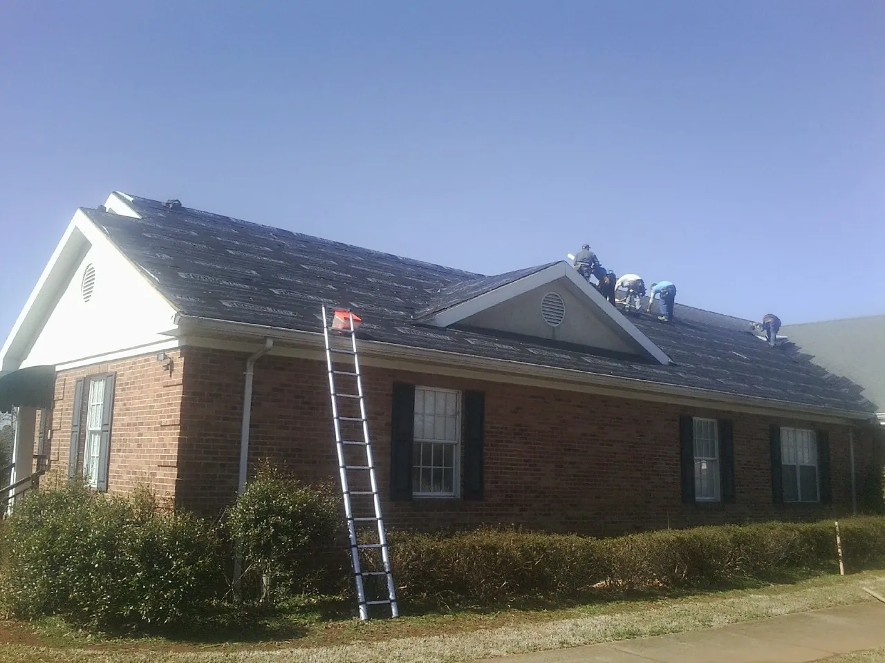 Crew tearing shingles off a brick ranch roof with a ladder set — Metal Roof Repair work by our crew in Beryl