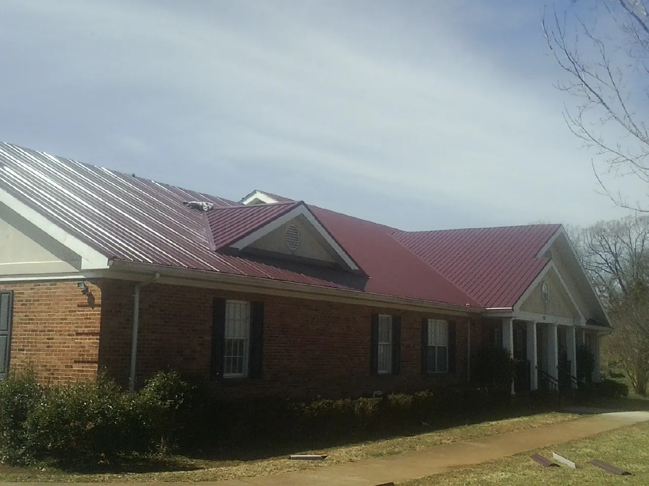 Red metal roof with gabled entries on a long brick building, from a Hail Damage Roof Repair job in Beryl