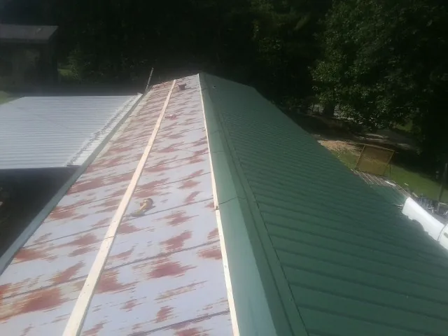 Old rusted panels beside newly installed green metal roofing — Wind Damage Roof Repair by Roofing Brothers in Beryl