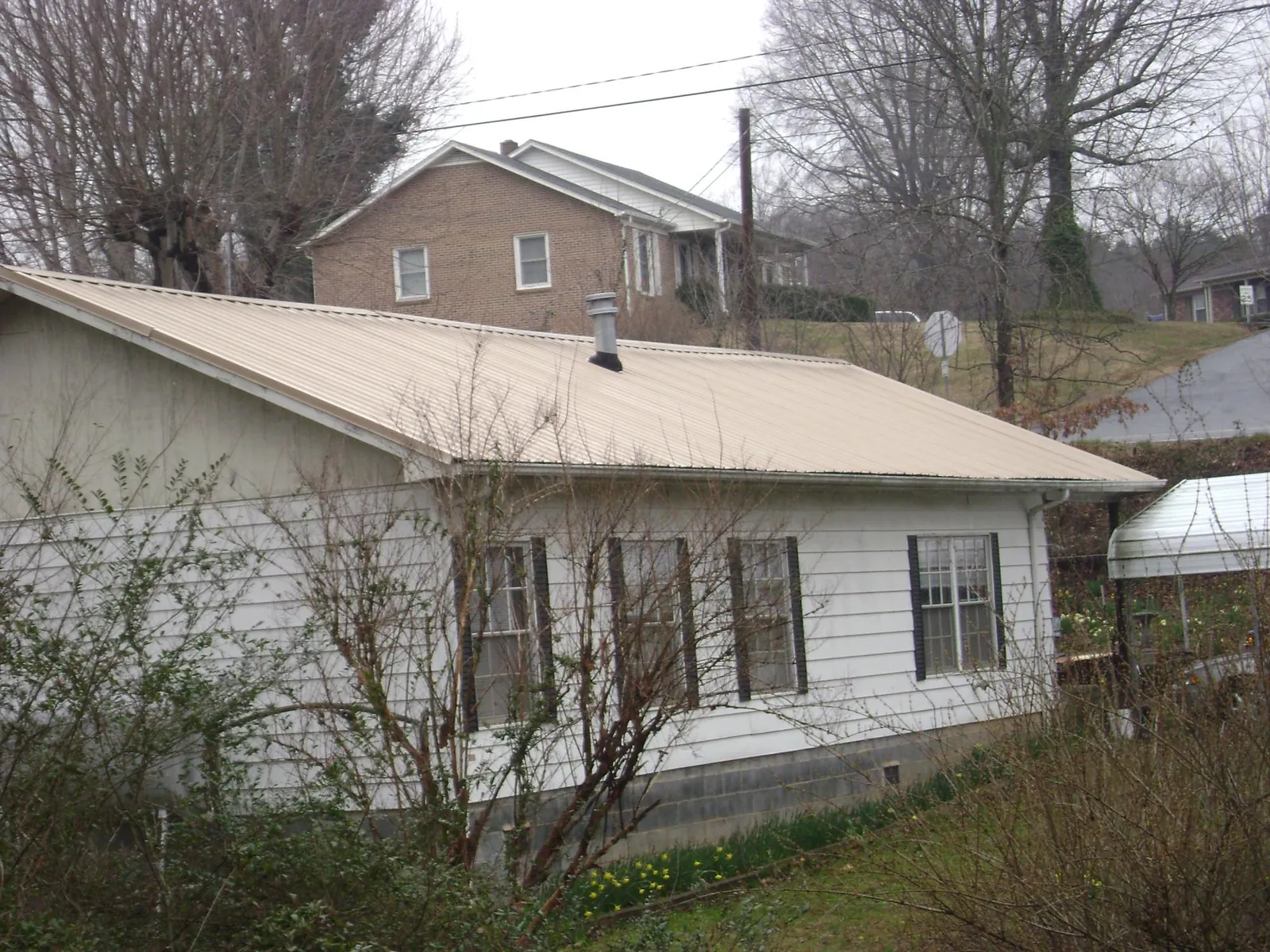 Tan metal roof on a white sided house set into a hillside — Commercial Roofing by Roofing Brothers in Beryl